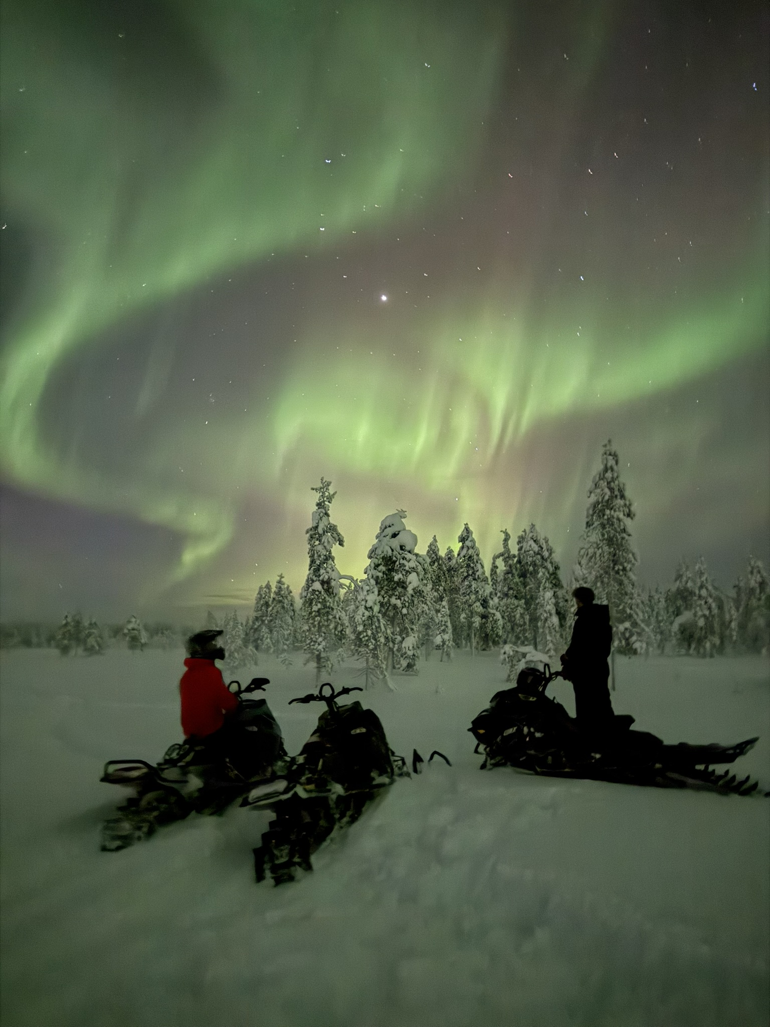 Snowmobile riders beneath the northern lights